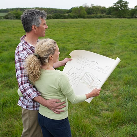How It Works couple looking at house plans in a field